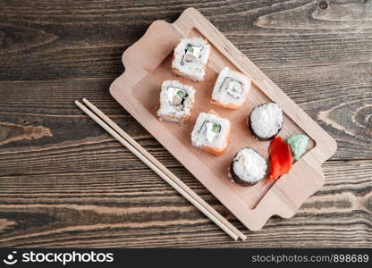 three different kinds of Japanese rolls with wasabi and ginger on bamboo tray on beautiful wooden background