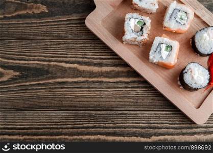 three different kinds of Japanese rolls with wasabi and ginger on bamboo tray on beautiful wooden background