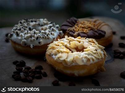 Three doughnuts covered with Almendras, Cookies and creme and Choco peanut butter on wooden cutting board. The concept of delicious glazed donuts, Space for text, Selective Focus.