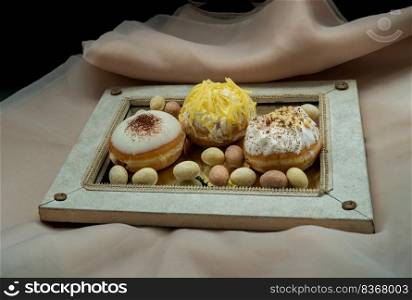 Three doughnuts covered with Cookies and Creme, Butter Cheese, Cappuccino Franco and White chocolate coated almonds with its reflection on mirror with pink background. The concept of delicious glazed donut, Selective Focus, Space for text, Selective Focus.
