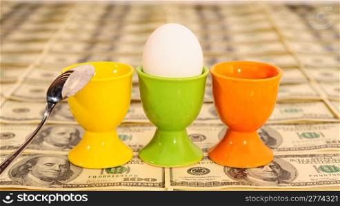 Three Eggs In Eggcups On Background With Many American Hundred Dollar Bills.
