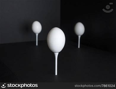 Three eggs standing on golf tees are highlighted against a black background.