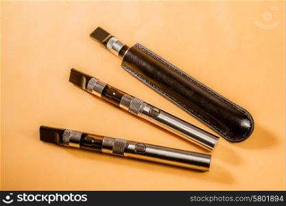 Three electric cigarettes lie next to each other on a yellow background. One of the cigarettes is in a black leather pouch.