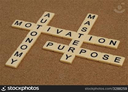 three elements of true motivation - mastery, autonomy, purpose - crossword with ivory letter blocks on cork board