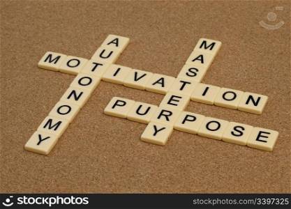 three elements of true motivation - mastery, autonomy, purpose - crossword with ivory letter blocks on cork board