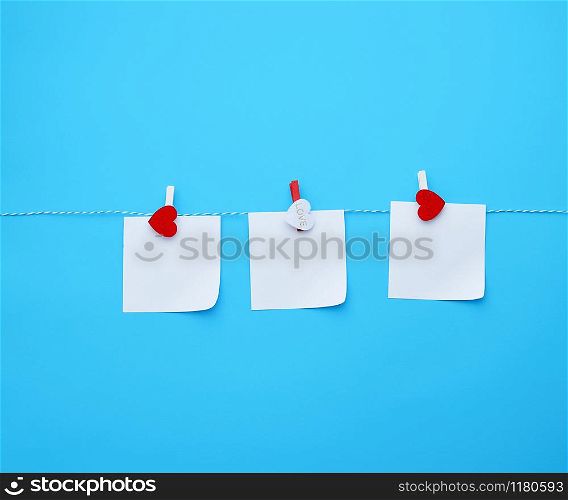 three empty square white paper sheets hanging on decorative clothespins, blue background