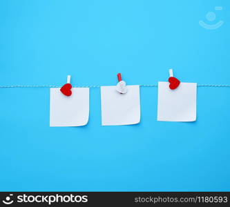 three empty square white paper sheets hanging on decorative clothespins, blue background