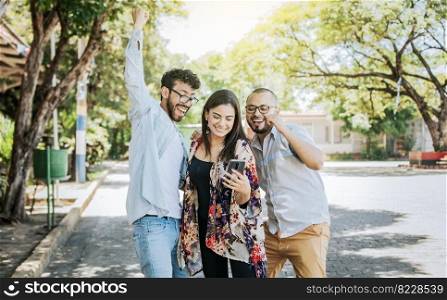 Three excited friends looking at the cell phone in the street. Three cheerful people looking at cell phone outdoors, Excited teenage friends looking at cell phone screen on the street