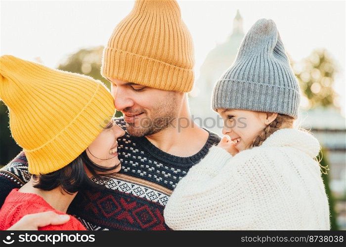 Three family members stand close to each other, look with eyes full of love and happiness, enjoy pleasant moments of being together, embrace each other. Family, happiness, relaxation concept