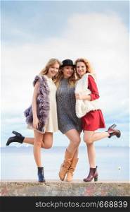 Three fashionable women having presenting pretty stylish outfits next to sea. Style, fashion, friendship concept.. Three fashionable woman against sea