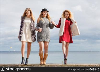 Three fashionable women having presenting pretty stylish outfits next to sea. Style, fashion, friendship concept.. Three fashionable woman against sea