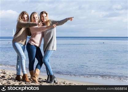 Three fashionable women sisters friends wearing sweaters during warm autumnal weather spending their free time on sunny beach. Fashion models outdoor. Three fashionable sister on the beach