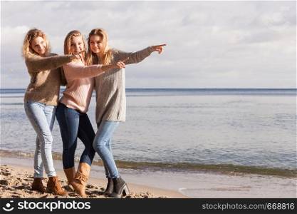 Three fashionable women sisters friends wearing sweaters during warm autumnal weather spending their free time on sunny beach. Fashion models outdoor. Three fashionable sister on the beach