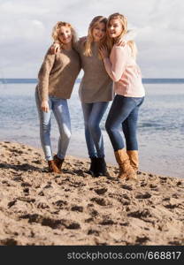 Three fashionable women sisters friends wearing sweaters during warm autumnal weather spending their free time on sunny beach. Fashion models outdoor. Three fashionable sister on the beach