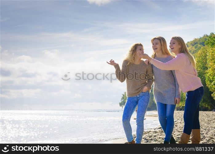 Three fashionable women wearing sweaters during warm autumnal weather pointing at copy space on sunny beach. Fashion models outdoor. Three fashionable models pointing outdoor