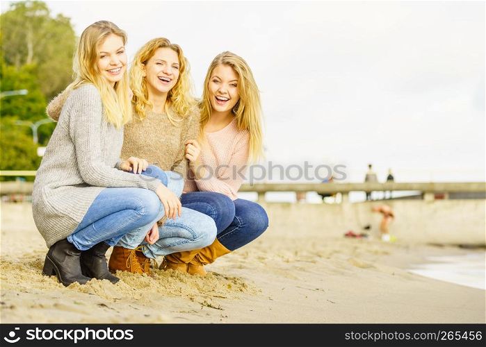 Three fashionable women wearing sweaters during warm autumnal weather spending their free time on sunny beach. Fashion models outdoor. Three fashionable models outdoor