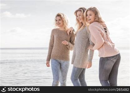 Three fashionable women wearing sweaters during warm autumnal weather spending their free time on sunny beach. Fashion models outdoor having fun.. Three fashionable models outdoor