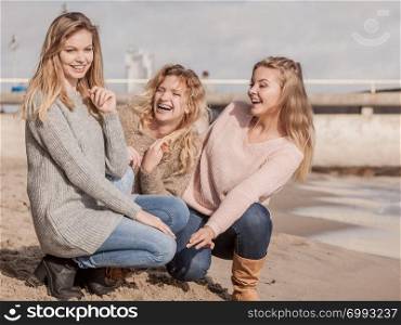 Three fashionable women wearing sweaters during warm autumnal weather spending their free time on sunny beach. Fashion models outdoor. Three fashionable models outdoor