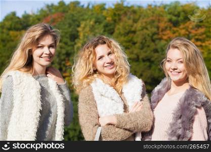 Three fashionable women wearing sweaters during warm autumnal weather spending their free time in park. Fashion models outdoor. Three fashionable models outdoor