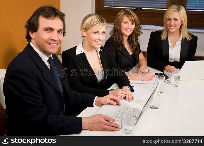 Three female executives and one male having a meeting in a boardroom - the focus is on the businessman in the foreground.