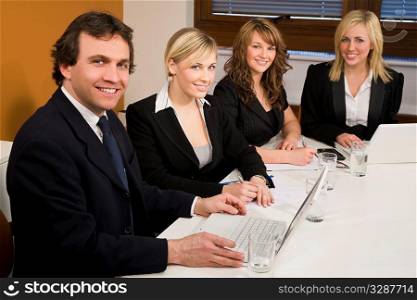Three female executives and one male having a meeting in a boardroom - the focus is on the businessman in the foreground.