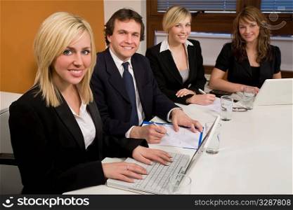 Three female executives and one male having a meeting in a boardroom - the focus is on the blond businesswoman in the foreground.