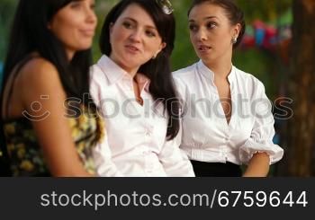 Three female friends taking a break on bench in the park, sharing stories