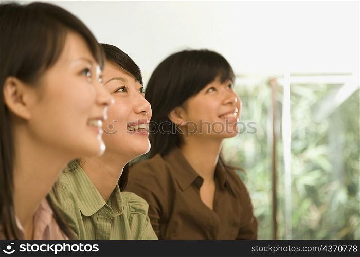 Three female office workers looking up and smiling