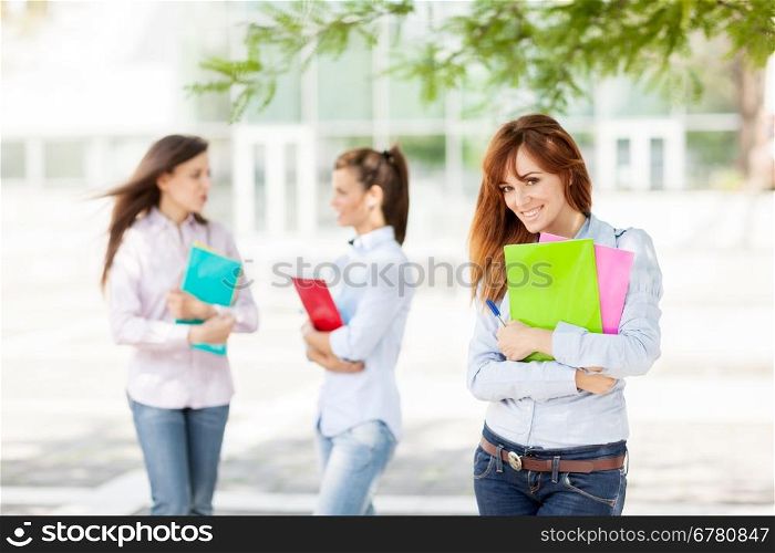 Three female students with notebooks are smiling