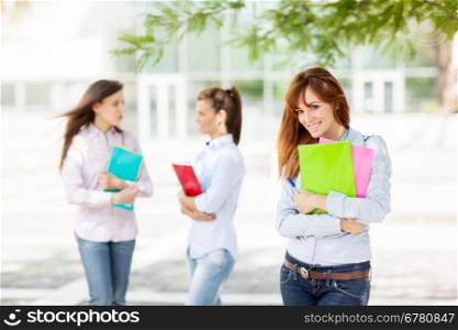 Three female students with notebooks are smiling