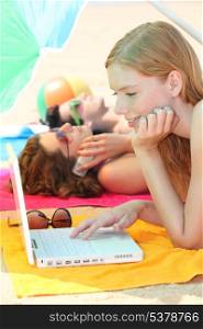 Three female teenagers with a laptop on the beach