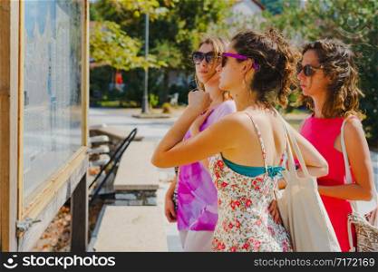 Three female tourist women looking at the map location on the info panel in the Greece tourist destination in a summer day on the vacation holiday information orientation