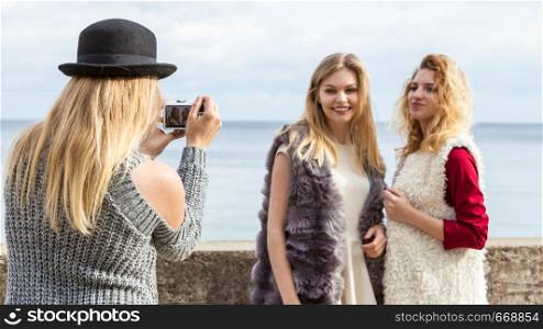 Three females friends having fun during outdoor photo session. Woman taking pictures of two during warm autumn weather.. Photo shoot of fashion models