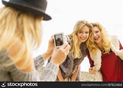 Three females friends having fun during outdoor photo session. Woman taking pictures of two during warm autumn weather.. Fun woman taking pictures of females