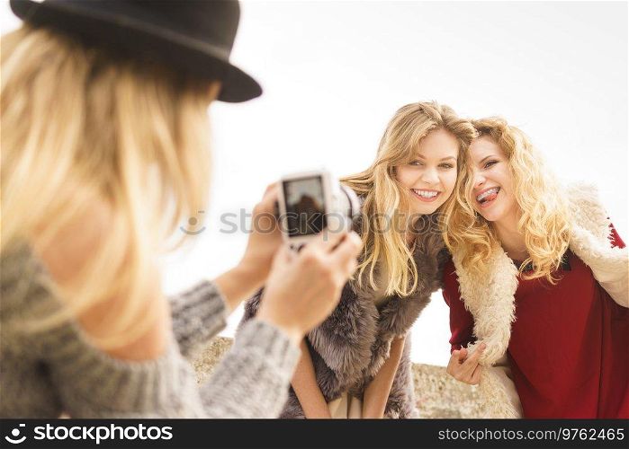 Three females friends having fun during outdoor photo session. Woman taking pictures of two during warm autumn weather.. Photo shoot of fashion models