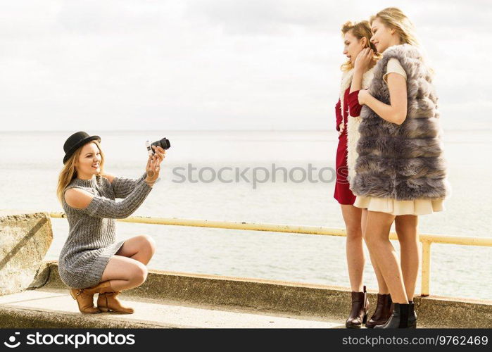 Three females friends having fun during outdoor photo session. Woman taking pictures of two during warm autumn weather.. Photo shoot of fashion models