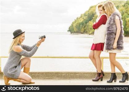 Three females friends having fun during outdoor photo session. Woman taking pictures of two during warm autumn weather.. Fun woman taking pictures of females