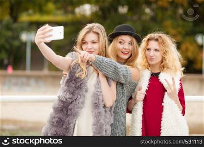 Three females taking selfies, having fun outdoor using smart phone to take photo.. Three women taking selfie outdoor