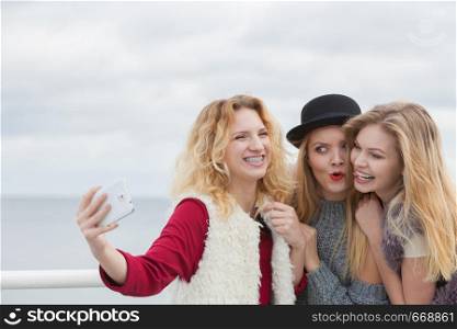 Three females taking selfies, having fun outdoor using smart phone to take photo.. Three women taking selfie outdoor