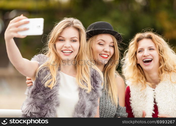 Three females taking selfies, having fun outdoor using smart phone to take photo.. Three women taking selfie outdoor