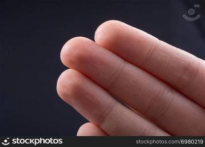 Three fingers of a child hand partly seen in black background