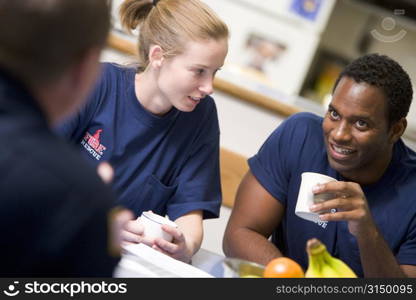 Three firefighters in break room drinking coffee and talking (selective focus)