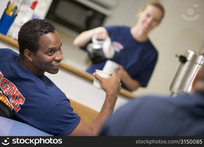 Three firefighters in break room with one getting coffee in background (selective focus)