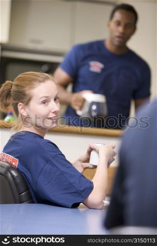 Three firefighters in break room with one getting coffee in background (selective focus)