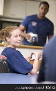 Three firefighters in break room with one getting coffee in background (selective focus)