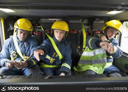 Three firefighters in fire engine wearing helmets with one pointing