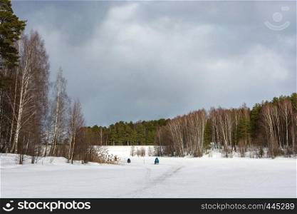 Three fishermen on the ice of a small river on a cloudy spring day, Russia.
