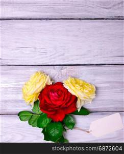 Three flowering roses and a white paper tag on a wooden background, empty space at the top