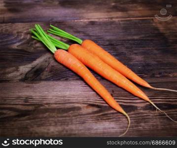 Three fresh carrots on a brown wooden background