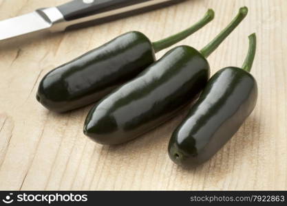 Three fresh green Jalapeno chili peppers on a cutting board